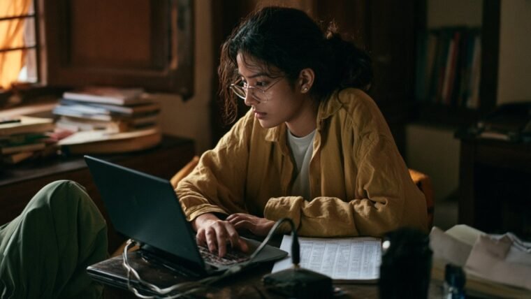 Woman at a desk checking a laptop with an ethernet cable running to a router