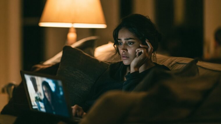 Woman on a night-time video call looking anxious, laptop screen lighting her face