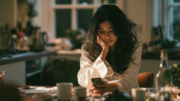 A young Indian woman using everyday AI apps on her smartphone at a kitchen table in morning light